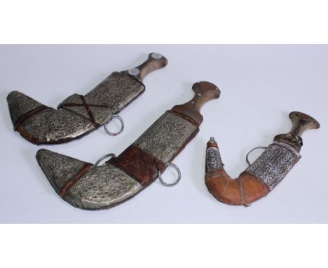 A Middle Eastern jambiya, 18cm curved blade, wooden grip, chased mounts to scabbard, 29cm long overall; others, similar (3) 
