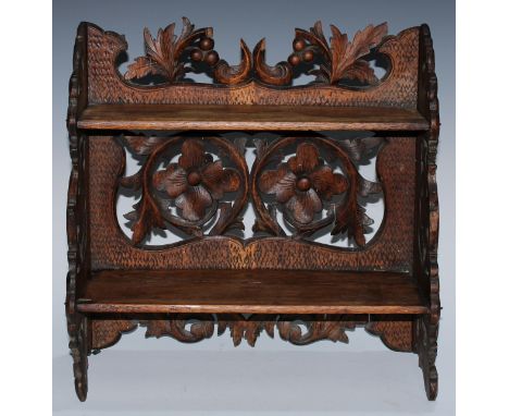 A Black Forest table-top two-shelf bookcase, the hinged sides restrained by hook-and-loops, carved in relief with leafy scrol