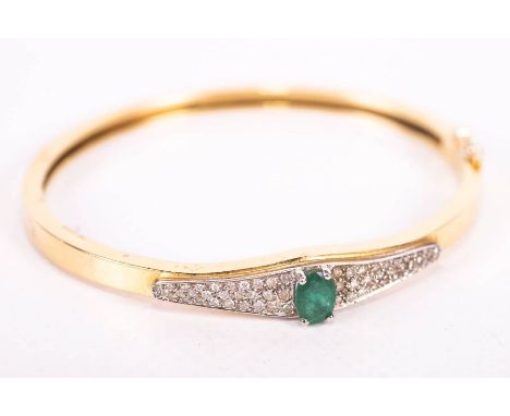 An emerald and diamond hinged bangle, in yellow metal, stamped 750 and 18ct. The central emerald is an oval mixed cut and mea