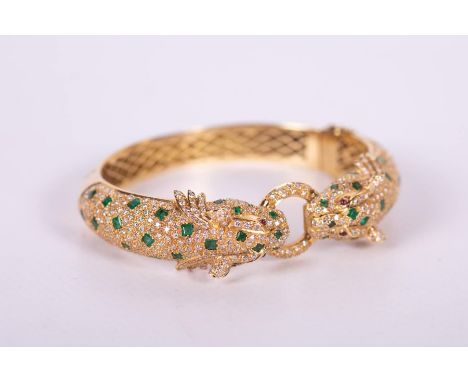 An 18ct diamond and emerald set double headed leopard hinged bangle, after Cartier.46.5 grams gross approximate weight.Hallma