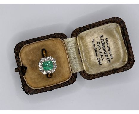 An emerald and diamond cluster ring in 18ct gold. The emerald is an octagonal step cut and measures approximately 6.92mm by 6