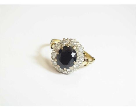 An 18ct gold sapphire and diamond cluster ring, designed as a central oval mixed cut sapphire claw set within a border of ten