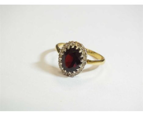 A garnet and diamond cluster ring, designed as a central oval mixed cut garnet claw set within a border of faceted diamonds, 