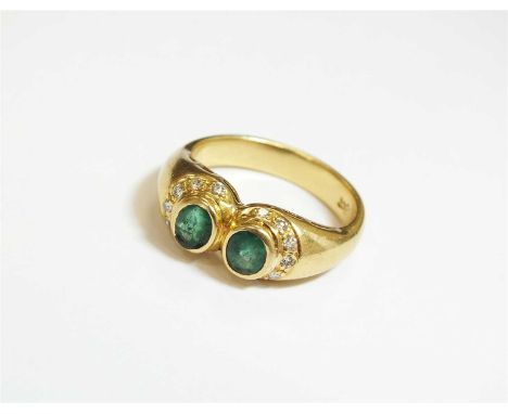 An emerald and diamond stylised torque ring, designed as two oval mixed cut emeralds collet set in yellow metal, each within 