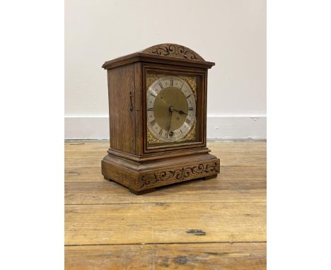 An Edwardian oak cased mantle time piece clock, the domed top over floral scroll carved frieze and stepped base, the silvered