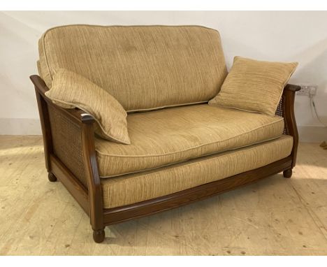 Ercol, a late 20th century stained elm framed two seat bergere sofa, with chinille upholstered squab and scatter cushions, on