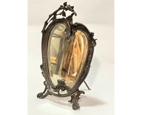 A cast metal Art Nouveau style table mirror with floral surmount and C scroll shaped bevelled glass encased plate, raised on 