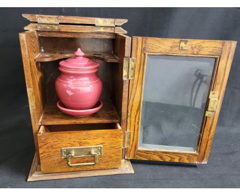 EARLY 20th CENTURY OAK SMOKERS CABINETwith a lift up lid, the interior with pipe rack, light plum coloured ceramic tobacco ja