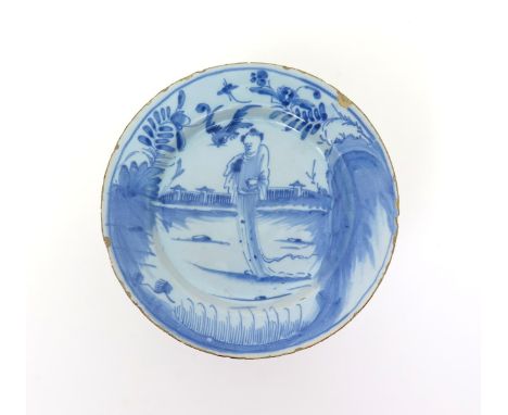 A Liverpool delftware plate  mid 18th century, painted in blue with a Chinaman standing before an ornamental fence, a bird an