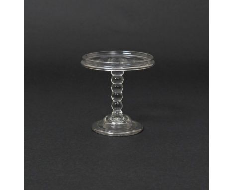 A glass patch stand  c.1740, the flat circular top with a vertical flange, raised on a bobbin-knopped stem above a domed and 