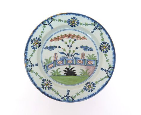 A delftware polychrome plate  c.1760, probably London, painted with feathery foliage stems issuing from a hatched fence, the 