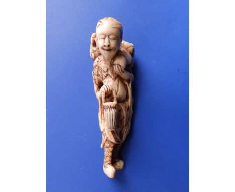 A Japanese ivory netsuke, depicting an elongated figure of an Immortal, carrying a basket in one hand and with a Shishi on hi