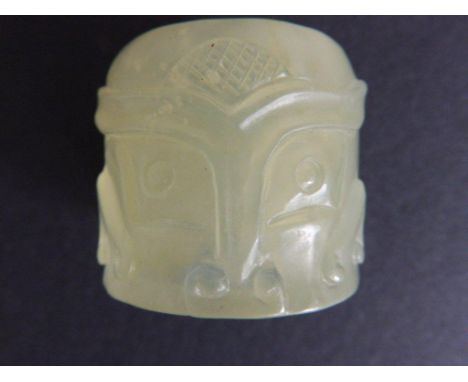 A Chinese celadon jade ring, carved with two warrior masks, 1.25”