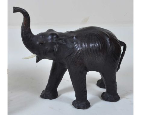 In the manner of Liberty &amp; Co - an early 20th century dark leather clad model of a baby elephant, its trunk raised and in