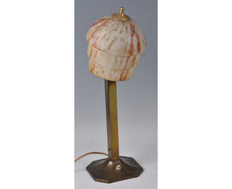 An Art Deco brass table lamp, having a circular stepped mottled glass shade, plain column to outswept faceted octagonal base,