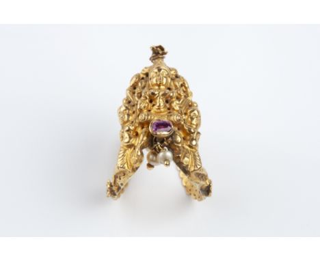 AN EASTERN GEM SET PANEL RING, the figural openwork panel highlighted with an oval-cut red stone in collet setting, issuing a