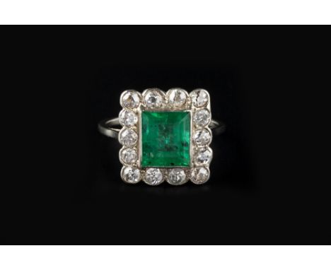 AN EMERALD AND DIAMOND CLUSTER RING, the rectangular step-cut emerald in millegrain collet setting, bordered by similarly set