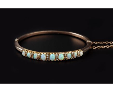 AN OPAL AND DIAMOND SET BANGLE, of hinged oval form, the tapered panel of graduated oval cabochon opals spaced by old and sin