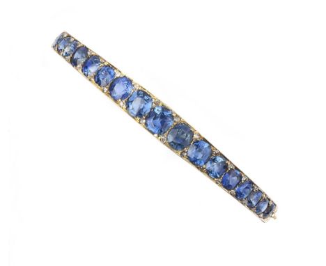 A SAPPHIRE AND DIAMOND SET BANGLE, of hinged oval trifurcated form, with scroll engraved sides, inset with a line of graduate