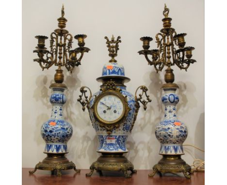A Dutch Delft earthenware and brass mounted three piece clock garniture, the garniture each having five candle lights, the cl