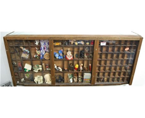 A wooden hanging display case with a quantity of miniature collectables including Wade Whimsies etc