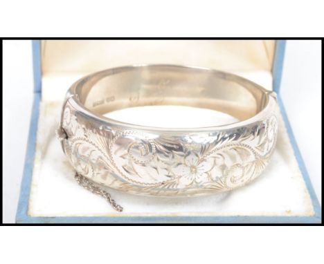 A silver hallmarked ladies rococo chased bangle with central push clasp and safety chain. Hallmarked for Birmingham, date let