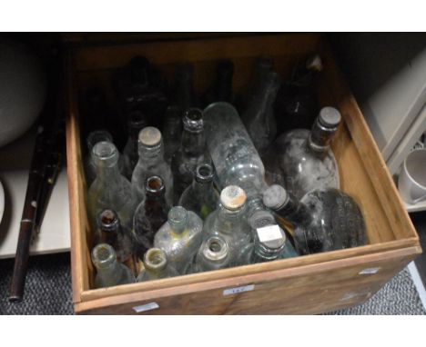 A wooden crate containing a selection of vintage and antique glass advertising bottles, including wine bottles and torpedo sh