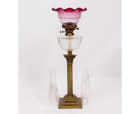 A 20TH CENTURY CORINTHIAN COLUMN BRASS OIL LAMP with cut glass reservoir, unassociated cranberry shade and two spare funnels,