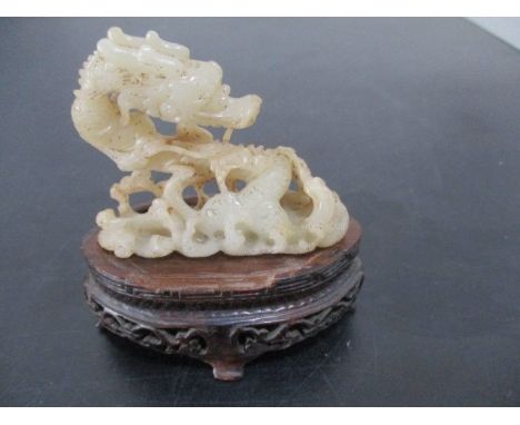 A carved jade figure of a dragon on ill fitting wooden stand