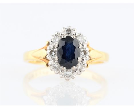 A hallmarked 18ct yellow gold sapphire and diamond cluster ring, set with an oval cut sapphire, measuring approx. 7x5mm, surr