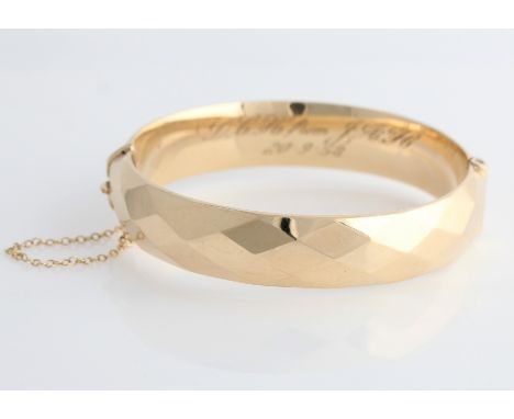 A hallmarked 9ct yellow gold hinged bangle, shaped with diamond pattern, personal engraving to inner band, with safety chain.