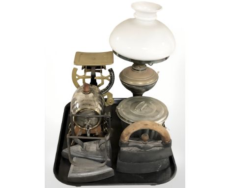 An oil lamp with opaque glass shade, a barrel drinks dispenser with matching cups, three irons, a scale, etc.