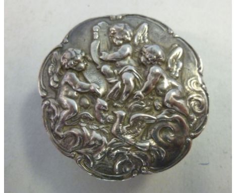 A silver pill box, the hinged cast lid decorated with three cherubs playing musical instruments  London 1980