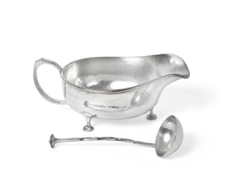 in the Arts and Crafts style, the sauceboat on three tapering block feet, with a hammered finish, the ladle with twisted hand