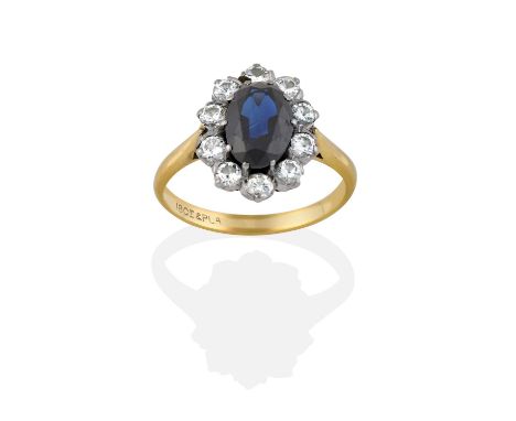 the oval cut sapphire within a border of round brilliant cut diamonds, in white claw settings, to a yellow tapered shoulder p