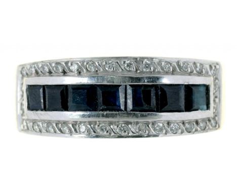 A SAPPHIRE AND DIAMOND SET 18CT WHITE GOLD RING, WITH CENTRAL LINE OF EIGHT CALIBRE CUT SAPPHIRES SURROUNDED BY ROUND CUT DIA