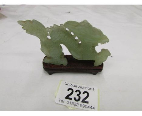 A jade dragon on wooden stand.