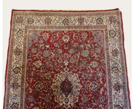 A LARGE PERSIAN CARPET worked with a central diamond motif within a scrolling surround against a red ground and multiguard bo