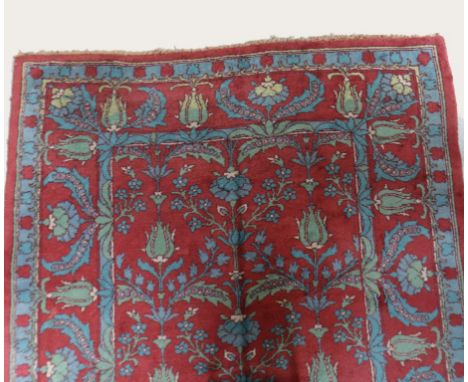 A DONEGAL STYLE ARTS AND CRAFTS CARPET worked with stylised tulip and leaf motifs in pale blues and greens against a deep red