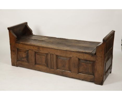 A PRIMITIVE OAK SETTLE with rising two plank top between rising shaped ends, one with integral cupboard, all above a four pan