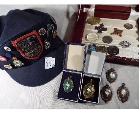 A cap with a collection of twenty enamel pin badges and similar attached and a case containing a further 14 badges and medall