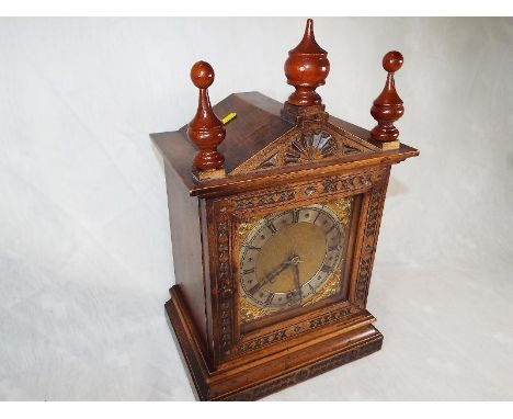 An Arts and Crafts styled mantel clock, the oak case having profusely carved decoration and turned finials, opening glazed do