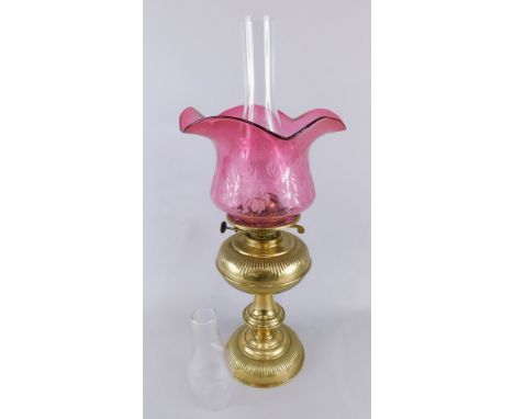 A Victorian brass lamp base, with Art Nouveau style cranberry tinted shade, a clear glass chimney, 54cm high and an extra sma