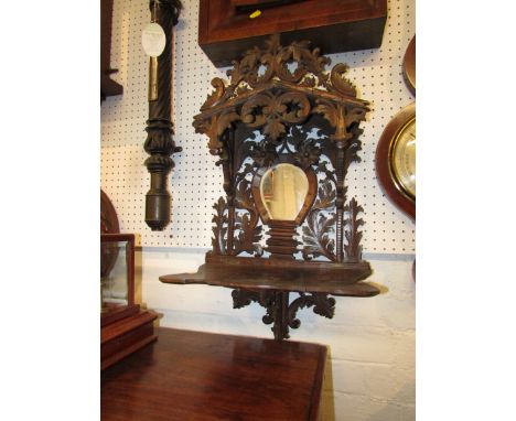 Black forest style carved dark wood wall bracket with single shelf, the apex canopy with foliate carving, the back with mirro