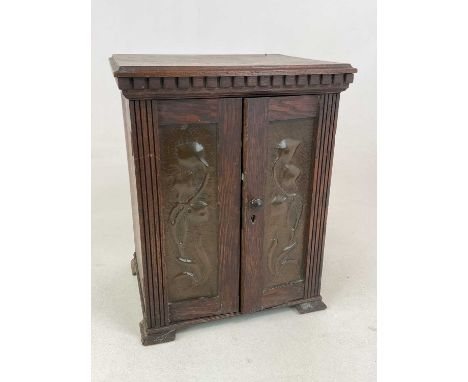 An Art Nouveau oak smoker's cabinet with decorated copper panels to the doors, pipe racks and a single drawer to the interior