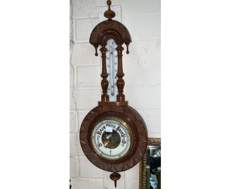 An Edwardian aneroid barometer with thermometer in carved walnut case 