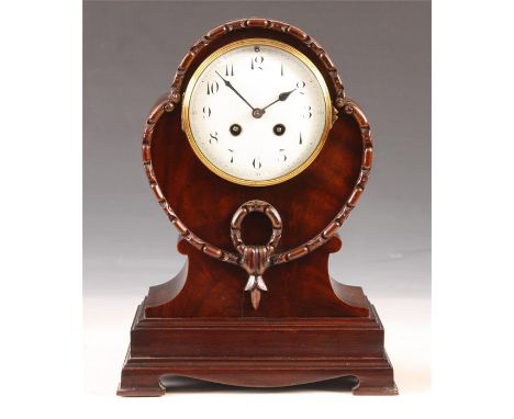 A late 19th Century Mahogany MANTEL CLOCK of shaped oval form with carved border on a skirted plinth base, the enamel convex 