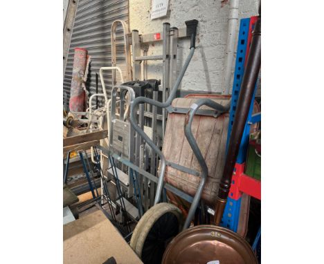 Various ladders, heavy duty packed shelving, 2 workbenches, wheelbarrow, a ladder stand-off. 