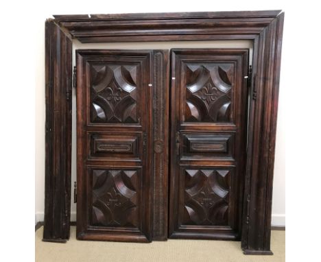 A pair of 19th Century French walnut doors with panelled and fleur de lys decoration together with surround (either from a sm