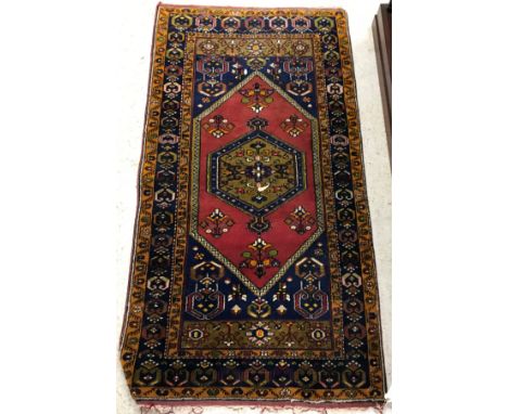 A Caucasian rug, the central panel set with lozenge shaped medallion on a red and blue ground, with stylised flower head deco